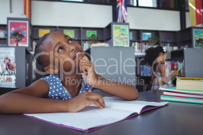 Thoughtful girl looking up at desk in library
