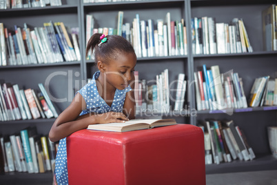 Girl reading book on ottoman in library