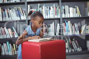 Girl reading book on ottoman in library