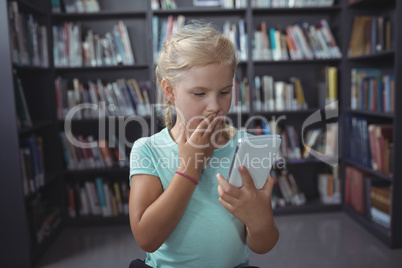 Surprised girl looking at smartphone in library