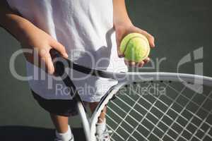 Midsection of girl holding tennis racket and ball