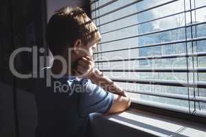 Boy looking through window glass of school