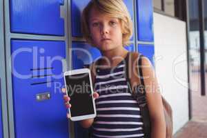 Portrait of boy holding mobile phone while standing by lockers