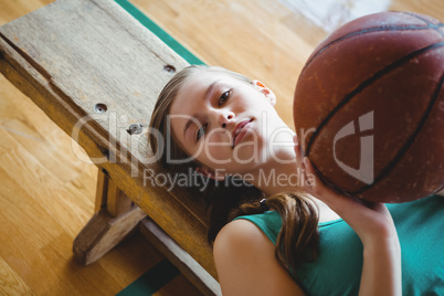 Portrait of female basketball player with ball lying on bench in court