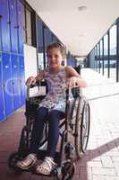 Portrait of smiling schoolgirl sitting on wheelchair in corridor