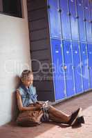 Elementary student using mobile phone while sitting by lockers