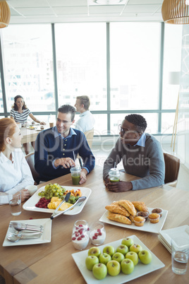 Smiling business colleagues having breakfast at office cafeteria