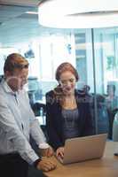 Businesswoman with colleague working on laptop at office desk