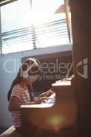 Concentrated girl wearing headphones while practicing piano by window