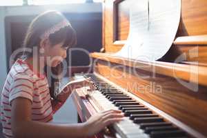 Side view of girl practicing piano in classroom