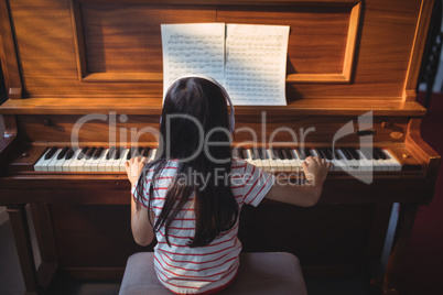 Rear view of girl practicing piano in classroom
