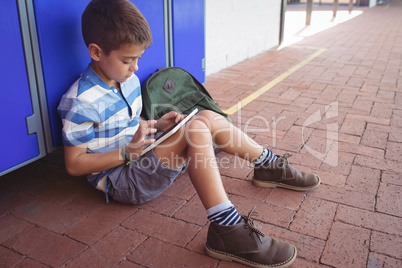 Boy using digital tablet while sitting by locker