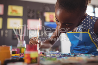 Concentrated elementary girl painting at desk