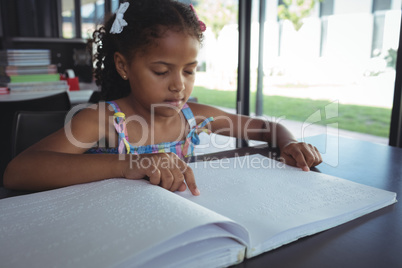 Girl reading braille at desk in library