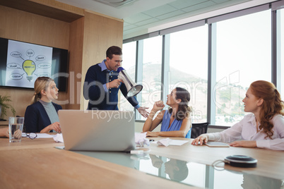 Angry businessman using megaphone in conference room