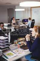 Businesswoman eating snack while colleagues working in creative office