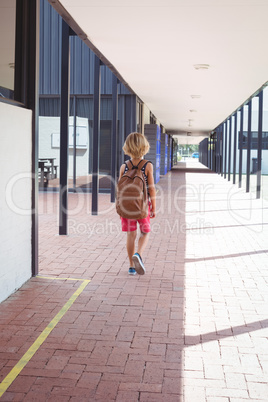 Rear view of schoolboy with backpack walking in corridor