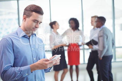 Businessman using mobile phone with colleagues discussing in background