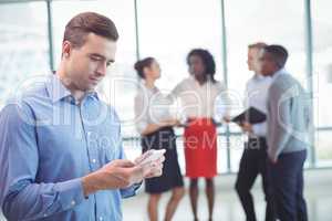 Businessman using mobile phone with colleagues discussing in background