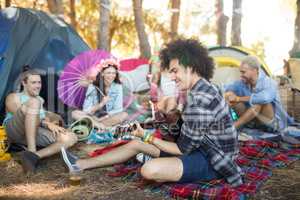 Young man playing guitar while sitting with friends at campsite