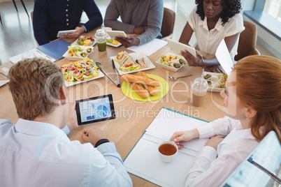 Businesswoman holding coffee cup while colleagues using digital tablets around breakfast table