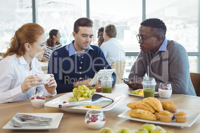 Businessman using digital table while sitting with colleagues in cafeteria