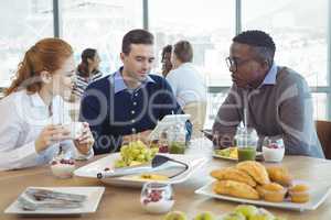 Businessman using digital table while sitting with colleagues in cafeteria