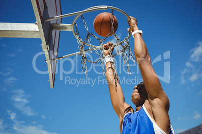Low angle view of teenager hanging on basketball hoop