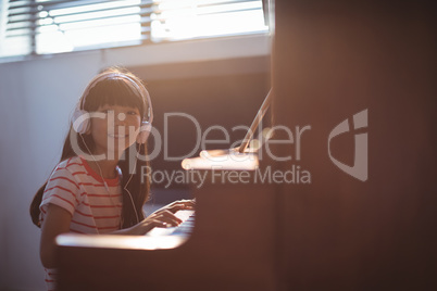 Portrait of smiling girl wearing headphones while practicing piano