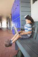 Side view of boy using laptop and virtual reality glasses while sitting on bench