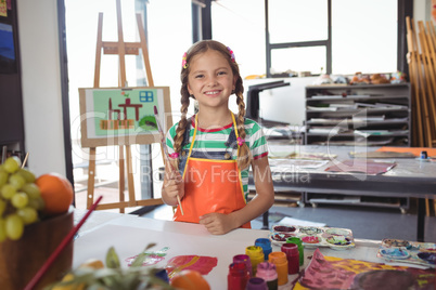 Portrait of happy girl holding paintbrushes
