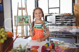 Portrait of happy girl holding paintbrushes