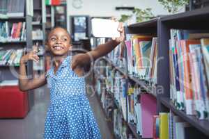 Smiling girl taking selfie by bookshelf in library