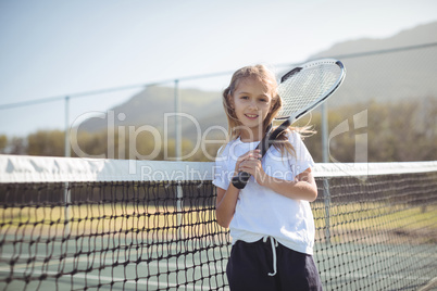 Smiling girl holding tennis racket while standing by net