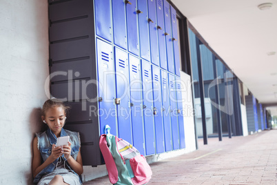 Elementary schoolgirl listening music through headphones while using mobile phone