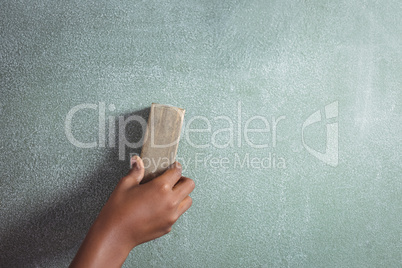 Cropped hand of student holding duster on blackboard