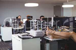 Low section of businesswoman relaxing while colleagues working in office