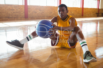 Portrait of teenage boy with ball sitting on floor