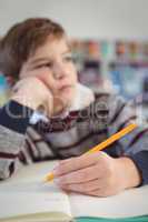 Thoughtful elementary schoolboy studing while sitting at desk