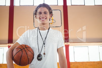 Portrait of happy male coach standing against basketball hoop
