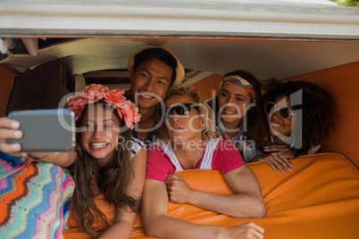 Smiling friends taking selfie while lying in camper van