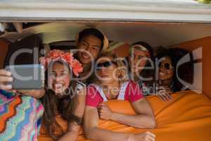 Smiling friends taking selfie while lying in camper van