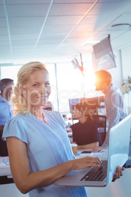 Portrait of businesswoman working on laptop with team in background