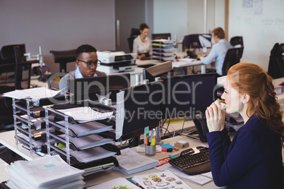 Businesswoman eating snack while colleagues working in office