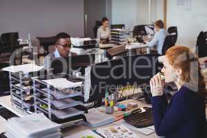 Businesswoman eating snack while colleagues working in office