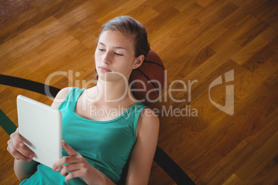 Female basketball player using digital tablet while relaxing in court