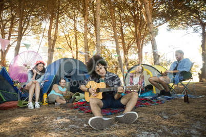 Young man playing guitar while friends sitting at campsite