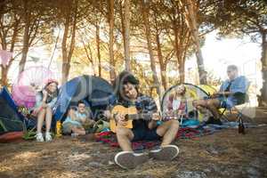 Young man playing guitar while friends sitting at campsite