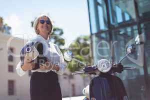 Businesswoman with helmet by motor scooter