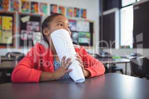 Thoughtful girl covering face with papers while sitting at desk